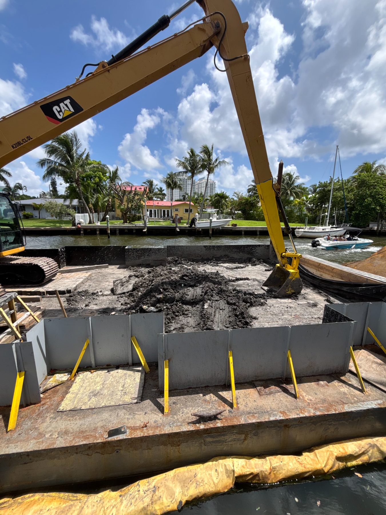 Long-reach excavator loading dredge spoil on a residential Miami slip